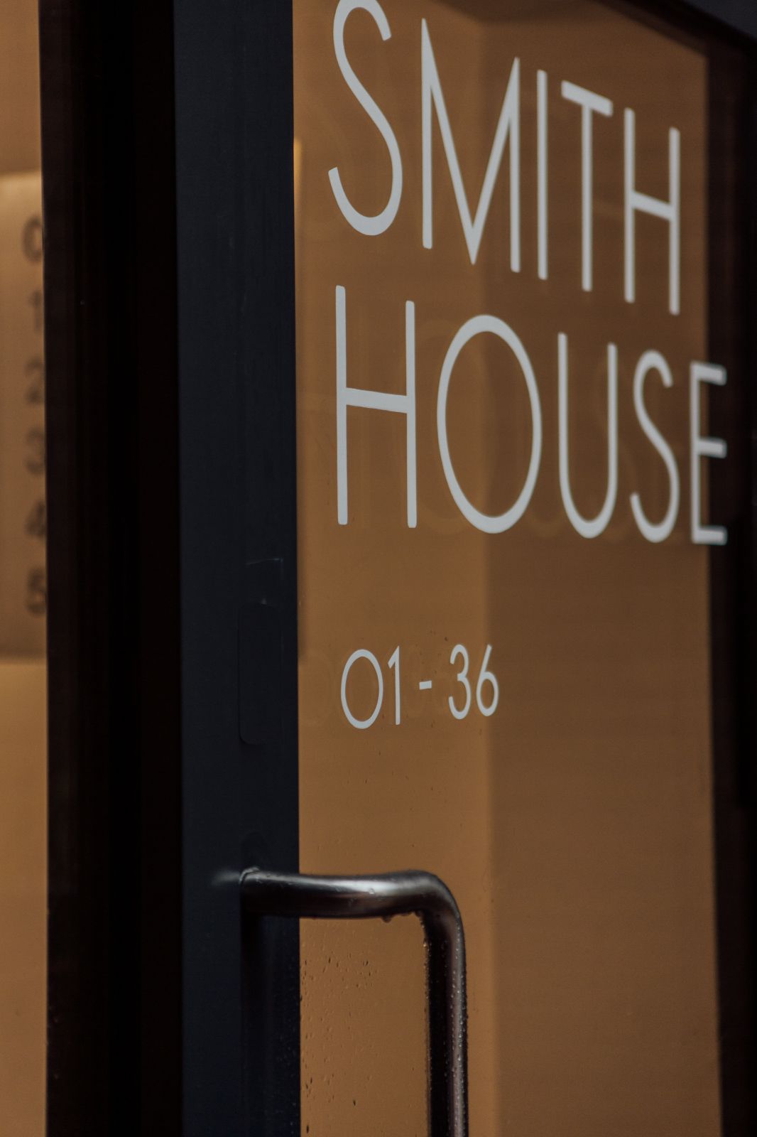 Contemporary glass entrance door with black frame and hand painted letters reading SMITH HOUSE 01-36.