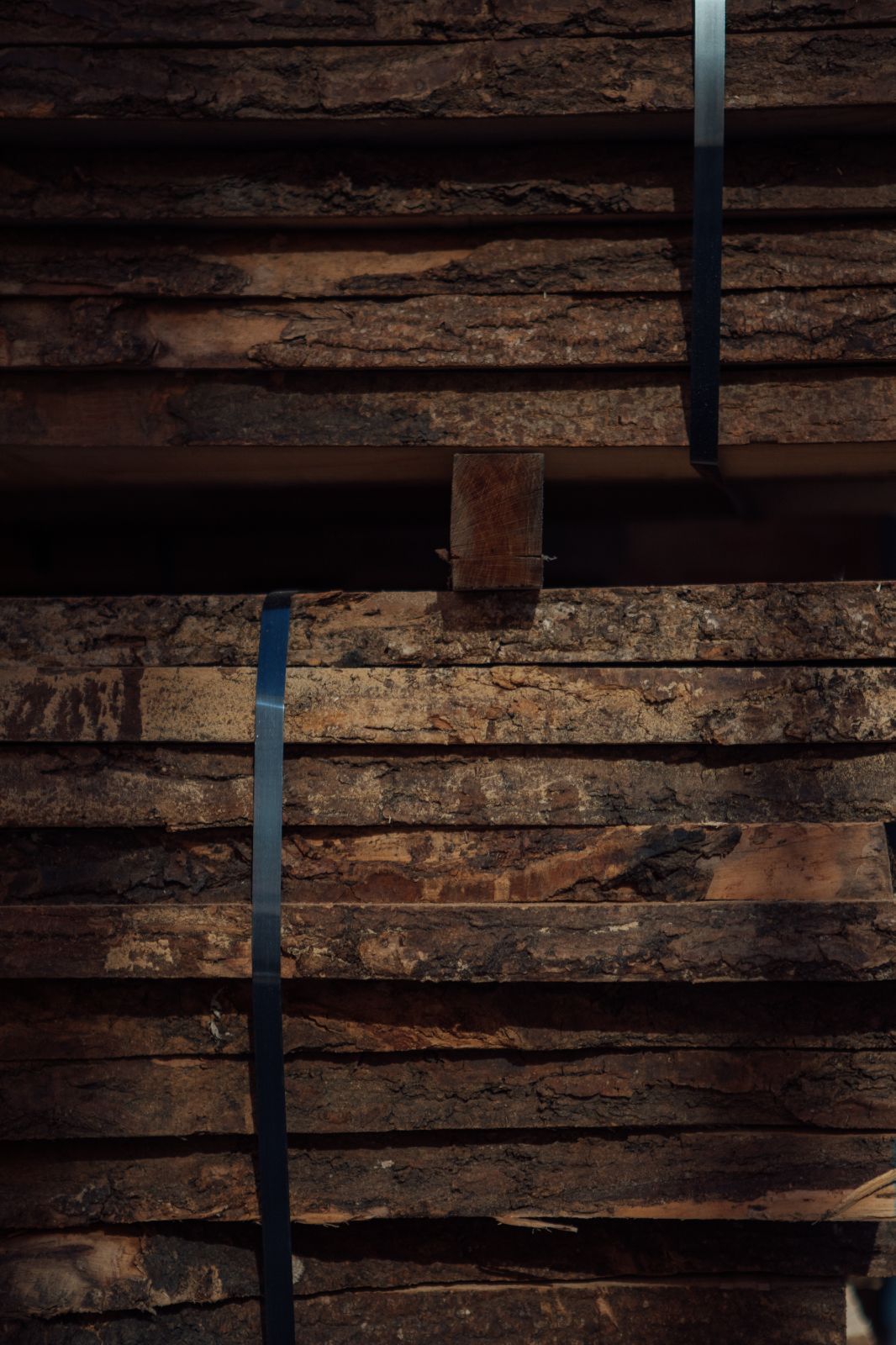 Close up of two stack of large wooden planks with bark and navy plastic straps holding the planks together.