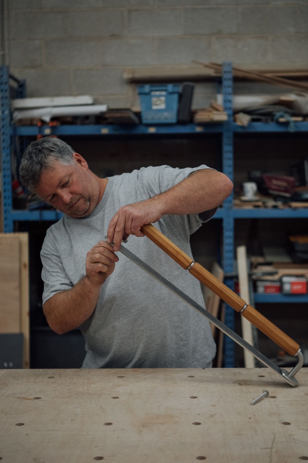 Craftsman assembling the long door handle in a workshop in Sheffield with blue unistrut shelving behind him.