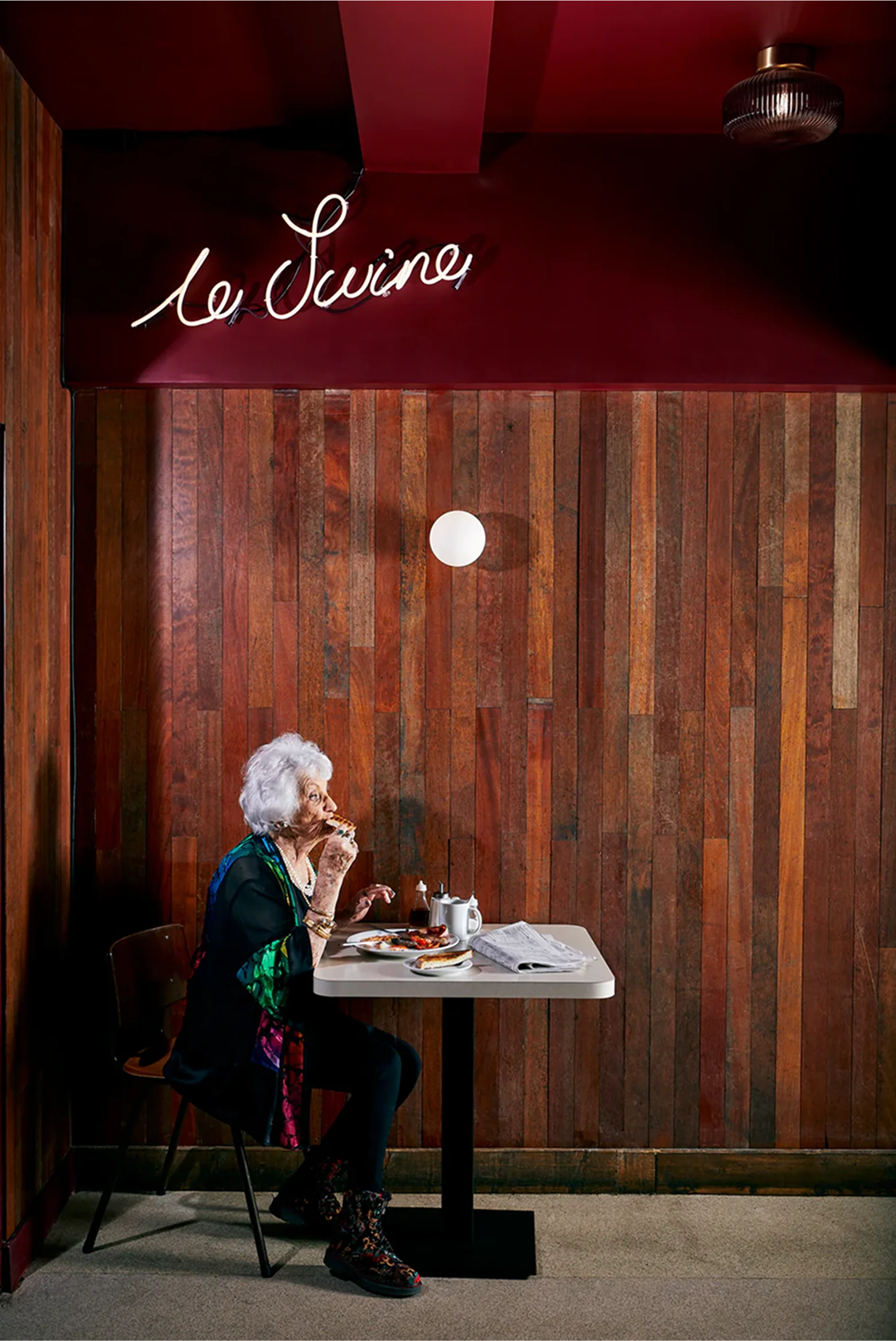 Old lady eating a bacon sandwich with a cup of tea at a table, interior shot