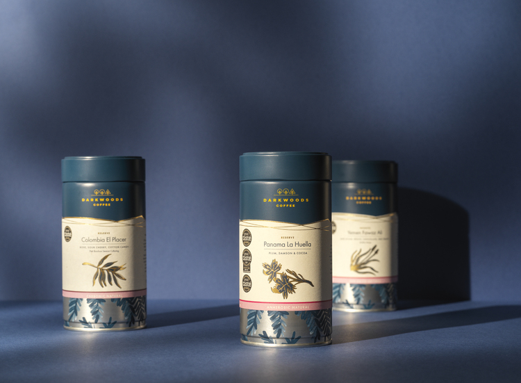 Three blue tins of Dark woods Reserve coffee on blue studio, still life background. Colombia El Placer, Panama La Huella