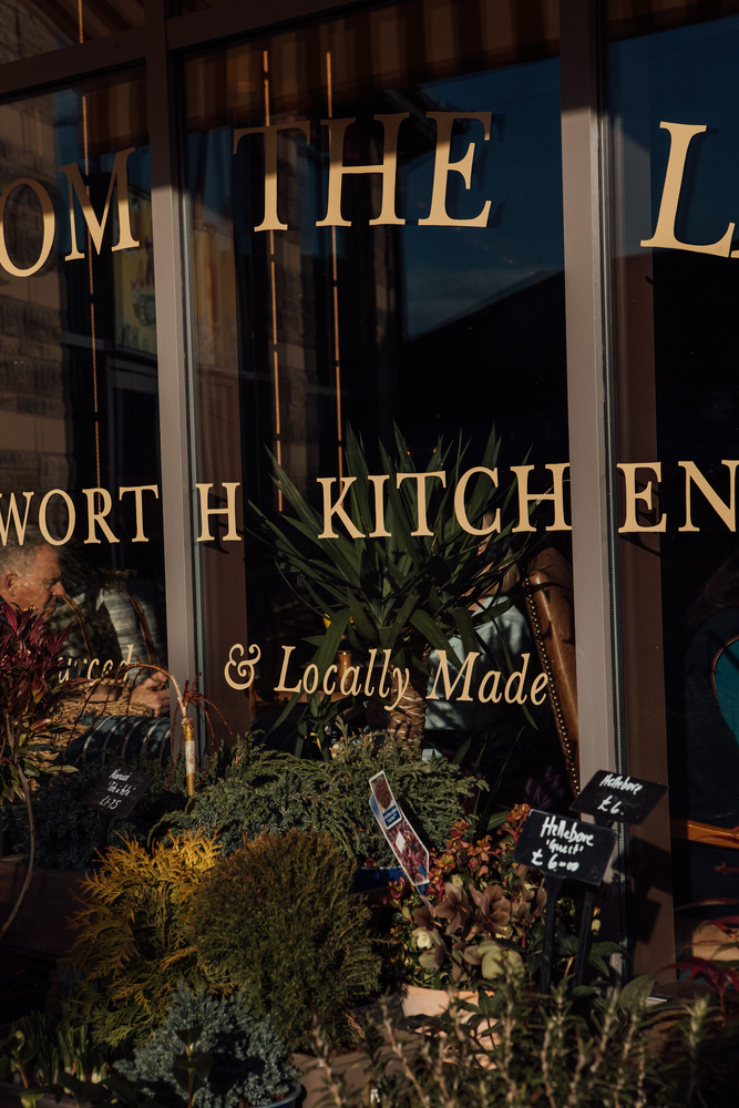 Close up of sign writing on Chatsworth Kitchen window. LOCALLY MADE. Flowers are for sale in the foreground. 