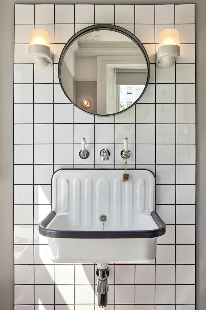 Vintage white basin with round, black-framed mirror above & twin lights either side. All set on white square tiles