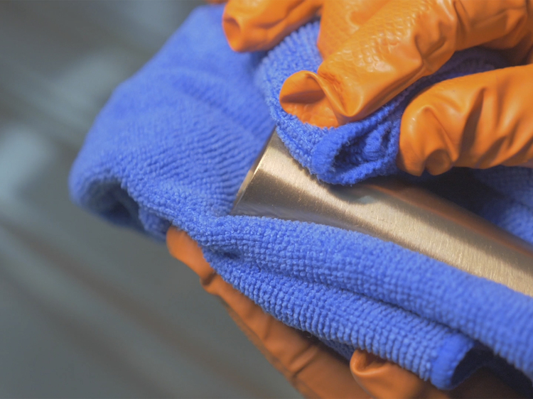 Metal tube coated with golden Physical Vapour Deposition coating being cleaned with a blue micro-cloth