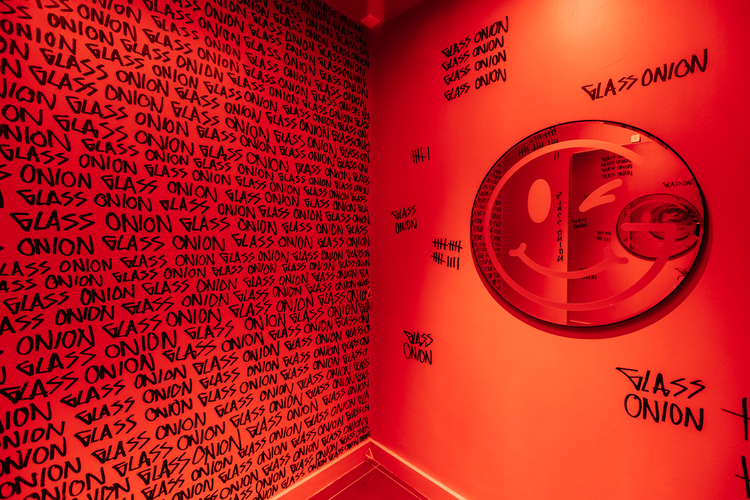 Red changing room with circular mirror with smiley face design & wallpaper repeating the words GLASS ONION