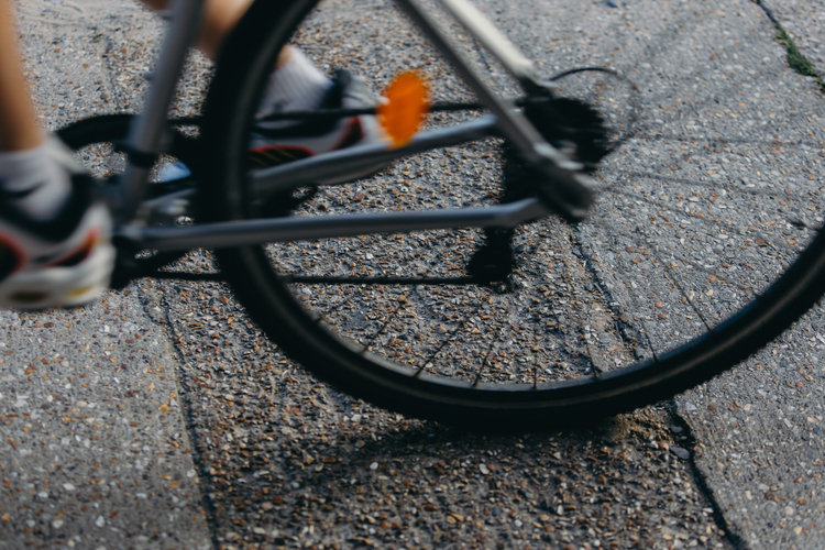 Close up of the back wheel of a bike & rider’s trainers just visible. The bike is slightly blurred as it moves past. 