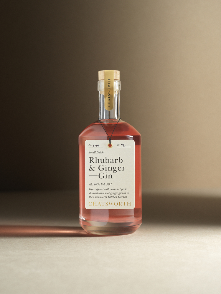 A bottle of pink small batch Chatsworth Rhubarb & Ginger Gin. Clear glass with a cork stopper, gold sticker and cream label.