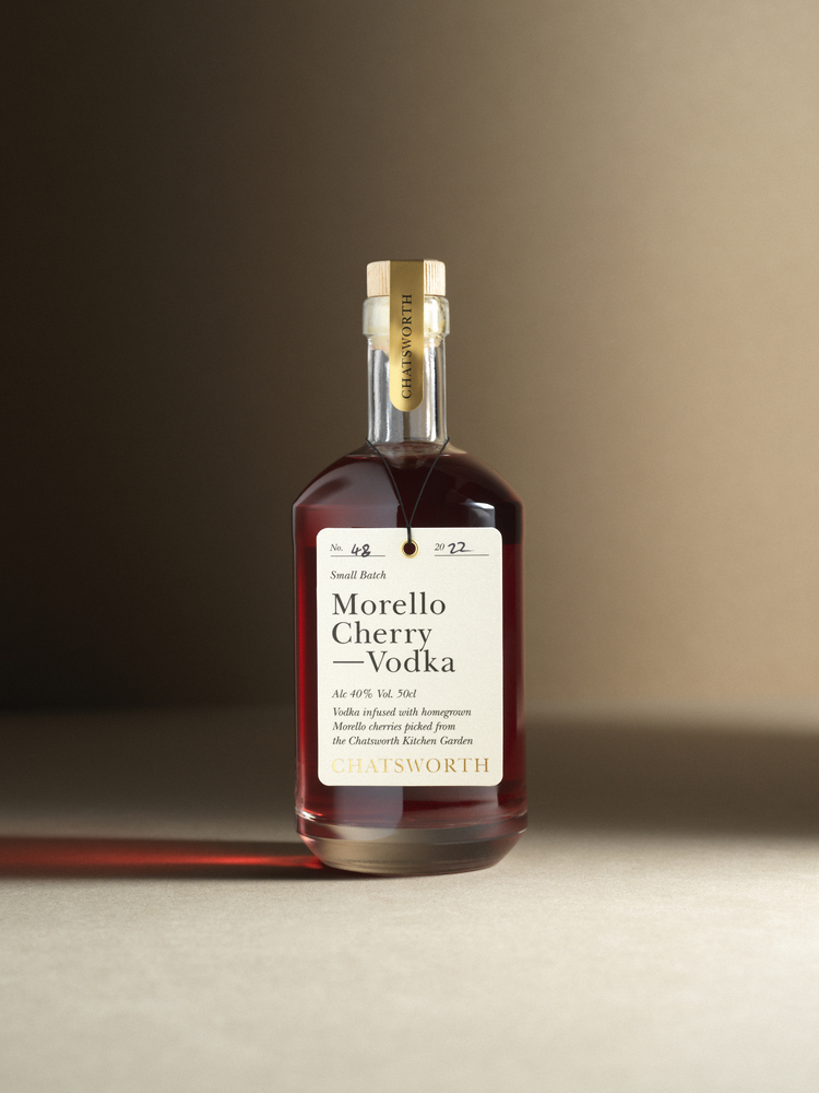 A bottle of red small batch Chatsworth Damson Gin. Clear glass with a cork stopper, gold sticker and cream label.